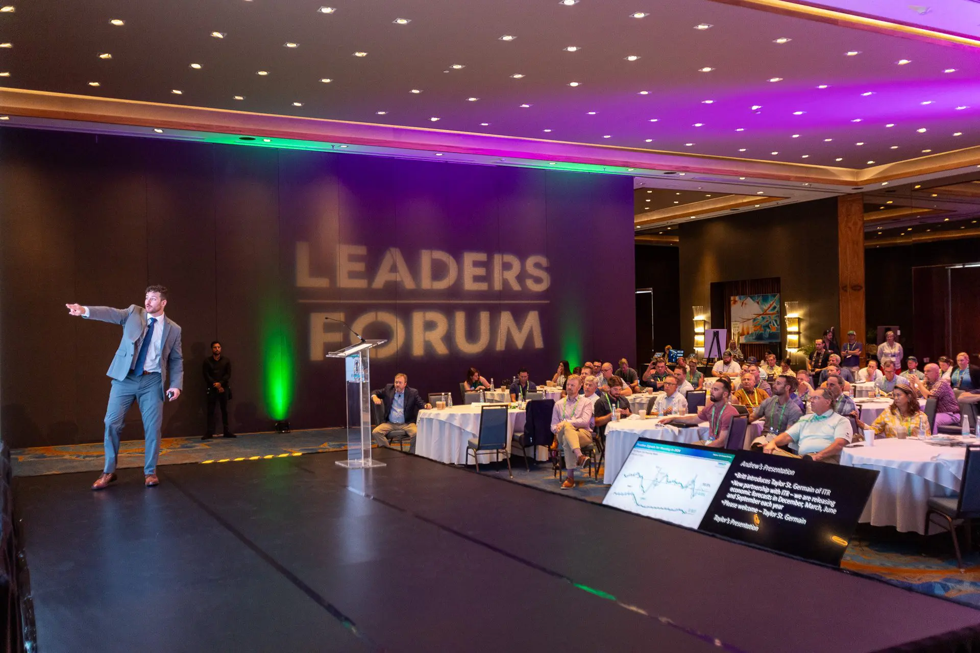 Orador con traje haciendo una presentación en el escenario durante un evento de liderazgo.
