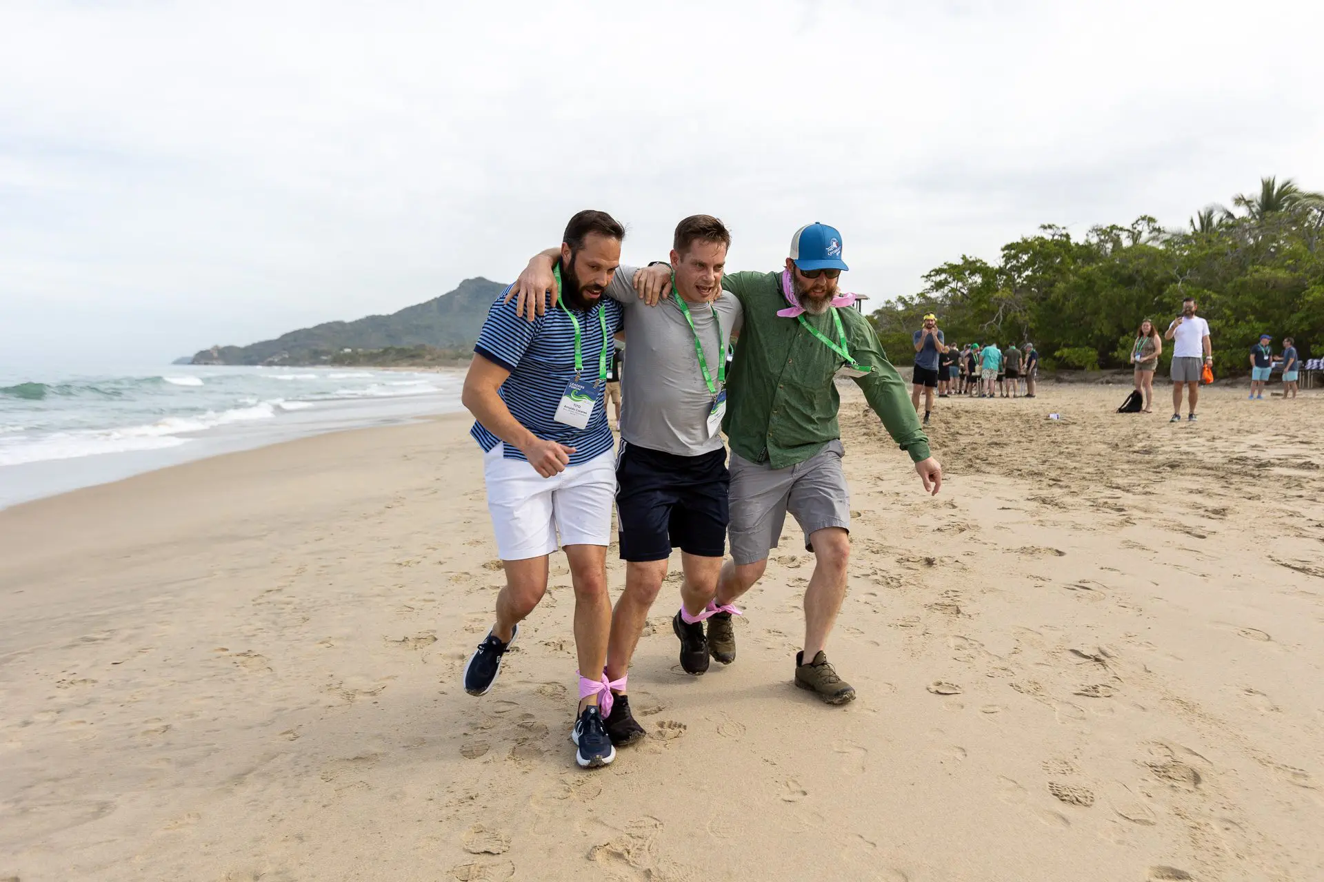 Grupo de hombres caminando por la orilla, abrazados.
