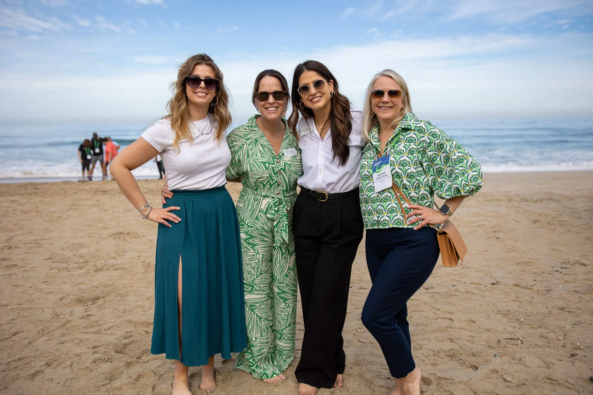 Cuatro mujeres con gafas de sol posando juntas en la playa.