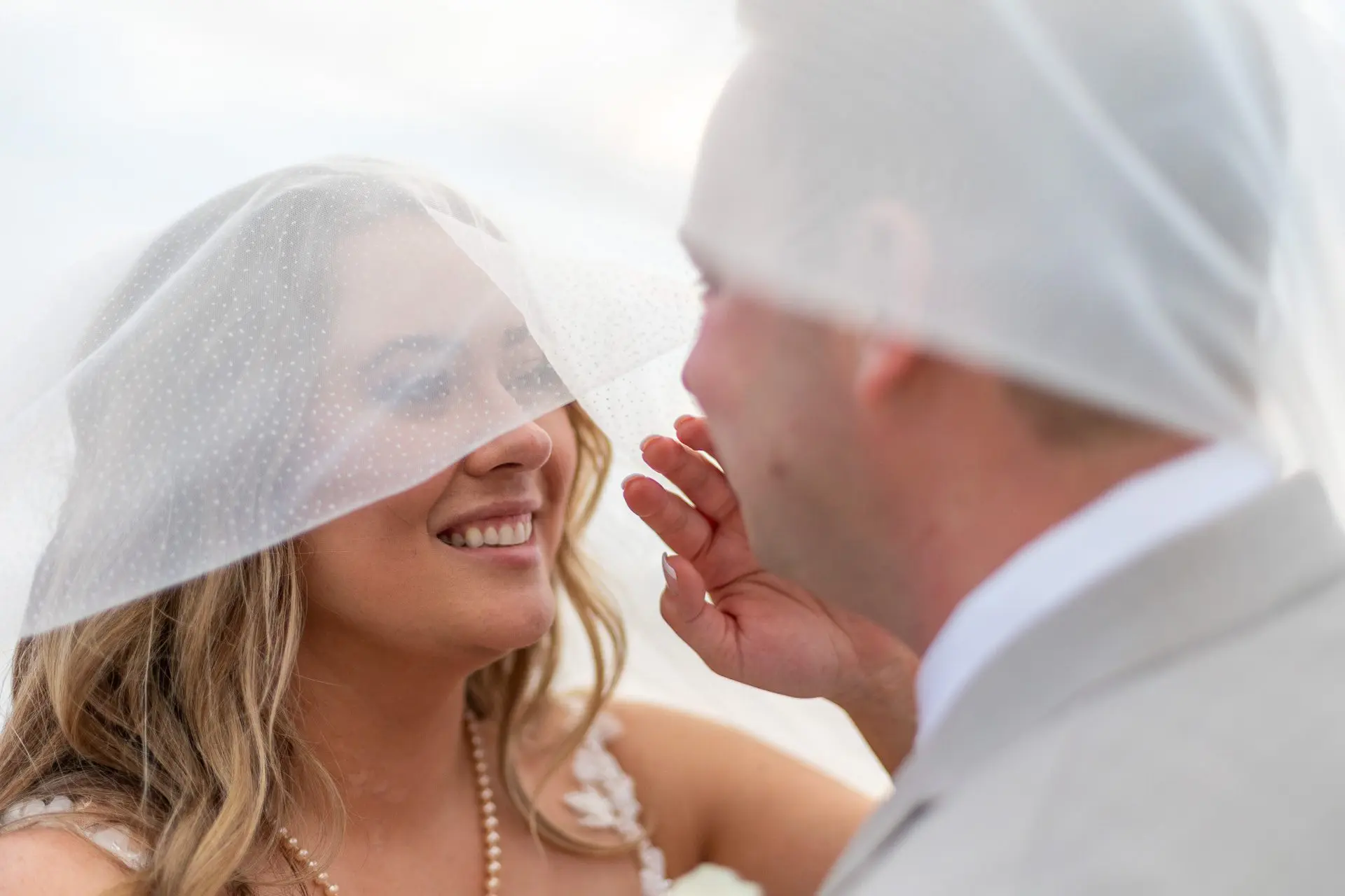 Os noivos sorriem um para o outro sob um véu de noiva em seu casamento em Puerto Vallarta