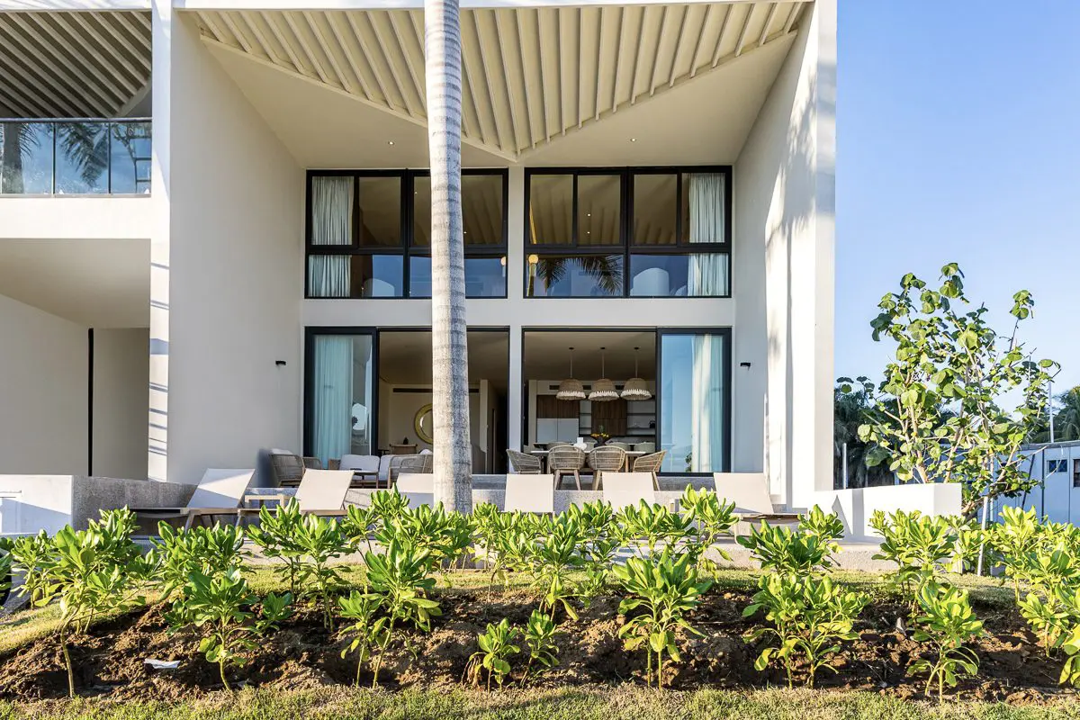 Exterior de vila moderna com um grande terraço coberto e paisagismo exuberante.