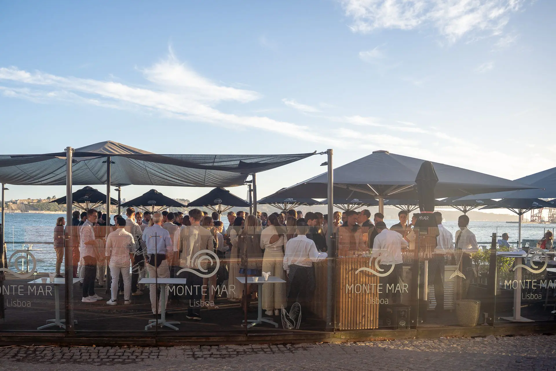 Foto de grupo de los asistentes disfrutando del ambiente nocturno, haciendo networking junto al agua con vistas al icónico horizonte de Lisboa.