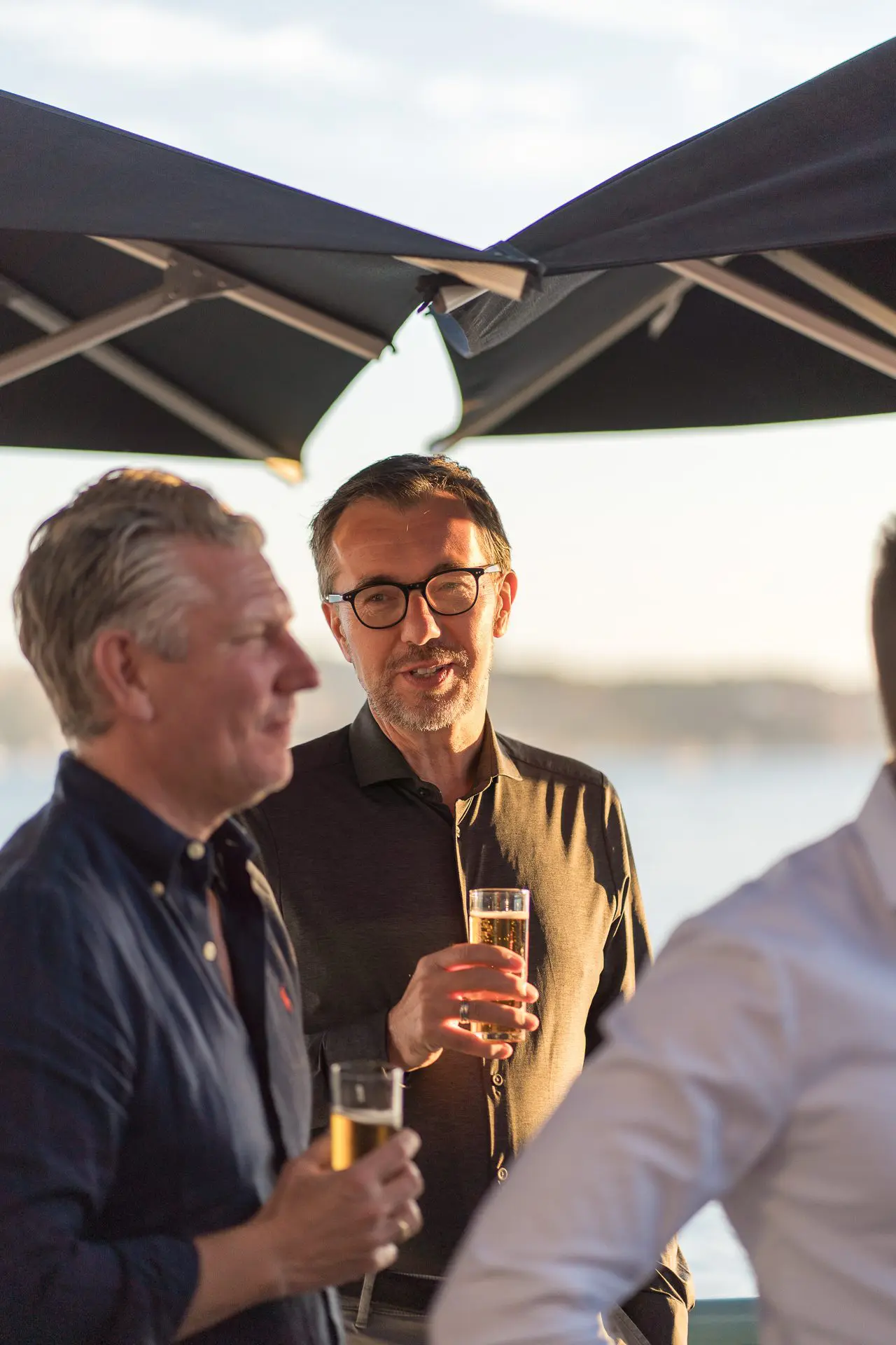 Los invitados se reúnen en un evento de networking frente al mar, tomando bebidas y participando en animadas conversaciones.