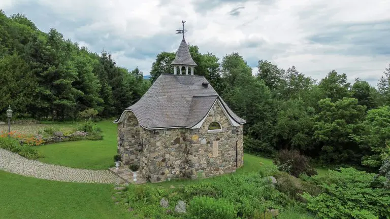 Una capilla de piedra rodeada de vegetación, frente a un cielo nublado.