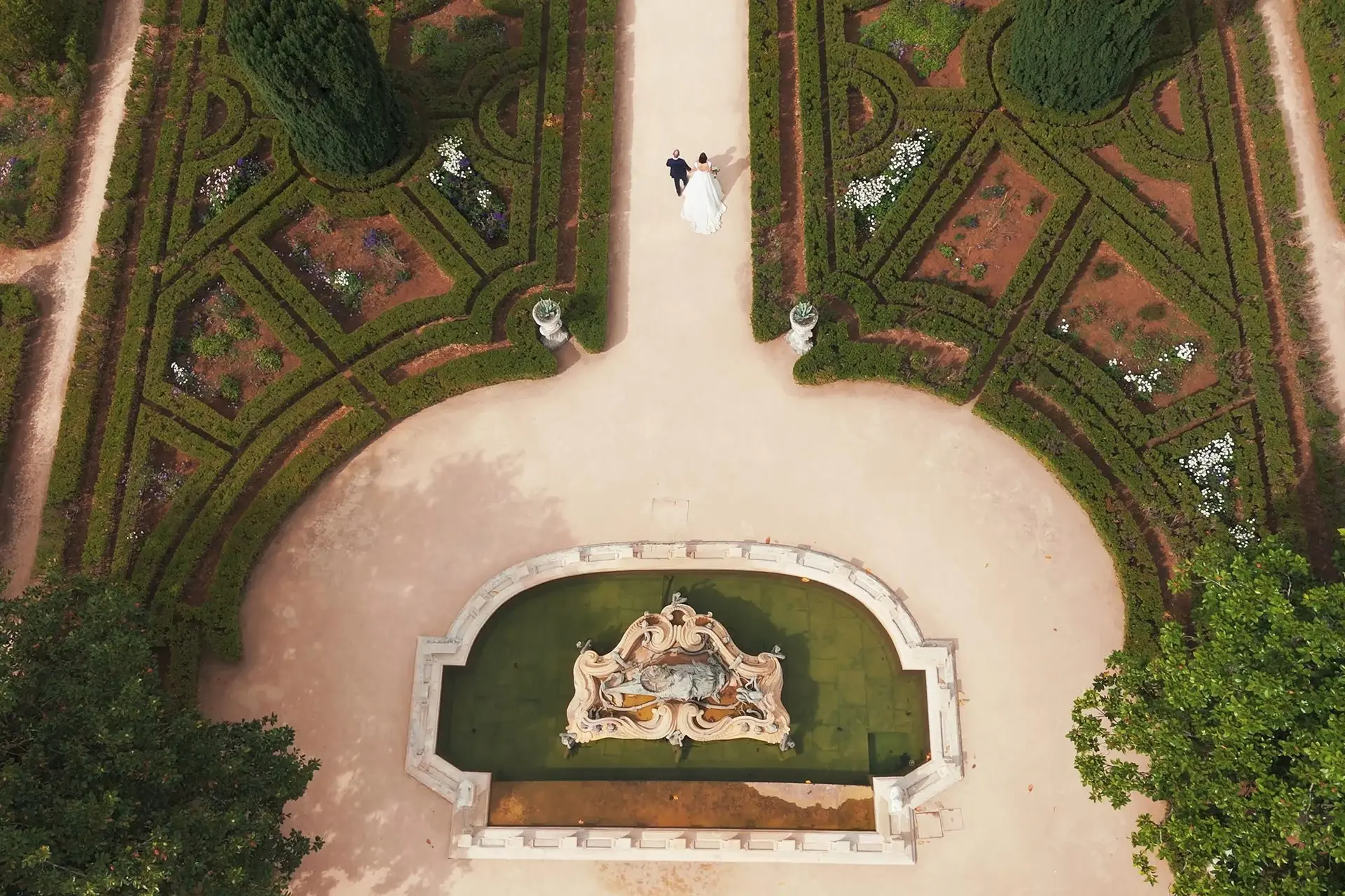 Drone shot of bride and groom walking through the gardens of Queluz National Palace in Lisbon, Portugal.