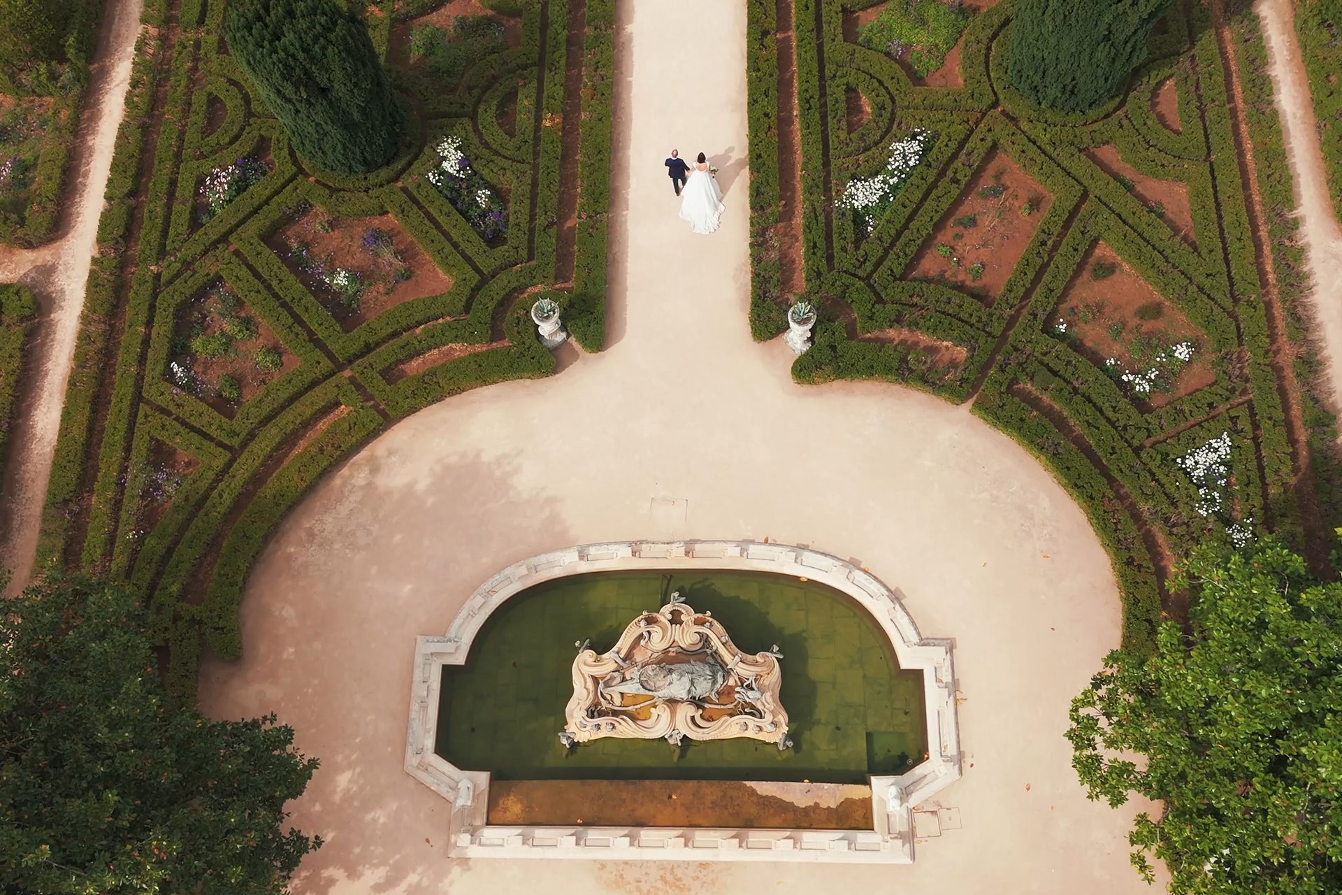 Drone shot of bride and groom walking through the gardens of Queluz National Palace in Lisbon, Portugal.